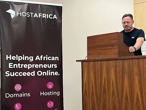 A HostAfrica speaker at a wooden lectern beside a HostAfrica banner at the Clawd and Claws meetup